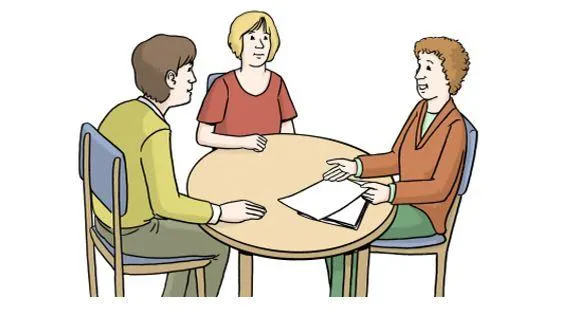 Ein Mann und zwei Frauen sitzen an einem Tisch und sprechen miteinander.